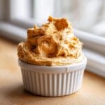 A close-up of fluffy, whipped honey butter, dusted with cinnamon, served in a small white ramekin.