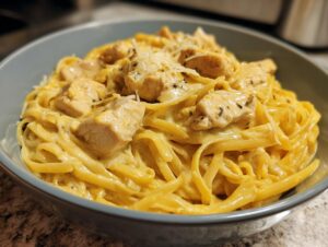 Close-up of creamy fettuccine chicken pasta topped with grated cheese in a light blue bowl.