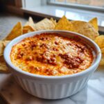 Close-up of a baked chili cheese dip topped with melted, bubbly cheese, served with tortilla chips.