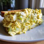 Close-up of a thick slice of amazing egg salad sandwich on toasted bread, showing creamy filling and celery chunks.