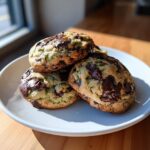 A stack of three delicious zucchini cookies loaded with large chunks of melted dark chocolate, sitting on a white plate.