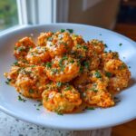 A close-up of crispy, saucy bang bang shrimp piled high in a white bowl, garnished with fresh parsley.