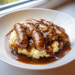 A close-up of a hearty serving of bangers and mash, featuring sausages smothered in onion gravy over creamy mashed potatoes.