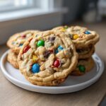 A stack of freshly baked, chewy m&m cookies loaded with colorful candies on a white plate.