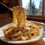 A fork lifts long strands of creamy caramelized onion pasta from a white bowl, topped with grated cheese.