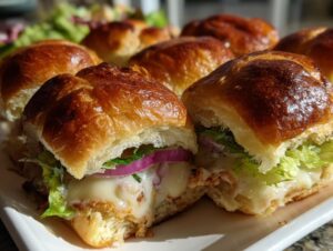 Close-up of two cheesy grinder sliders cut open, showing melted cheese, lettuce, and red onion on golden baked buns.