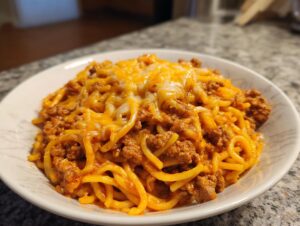 A close-up of a serving of cheesy taco pasta featuring spaghetti noodles mixed with seasoned ground beef and topped with melted cheddar cheese.