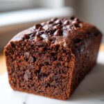 A close-up of a rich, dark chocolate zucchini bread loaf topped with chocolate chips.