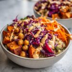 Close-up of a vibrant buddha bowl featuring quinoa, roasted sweet potatoes, shredded red cabbage, chickpeas, and a creamy tahini dressing.