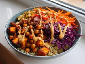 A vibrant, healthy buddha bowl featuring quinoa, roasted sweet potatoes, chickpeas, shredded carrots, red cabbage, and a creamy tahini dressing.