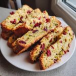 Several slices of golden cranberry pistachio biscotti packed with dried cranberries and green pistachios, served on a white plate.