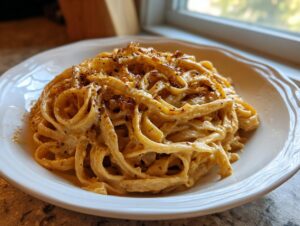 Close-up of creamy caramelized onion pasta tossed with wide noodles, served in a white bowl near a window.