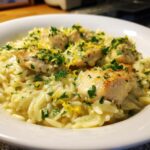 Close-up of creamy chicken pieces served over lemon orzo pasta, garnished with parsley and zest.