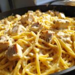 Close-up of creamy chicken pasta with chunks of seasoned chicken in a dark skillet.