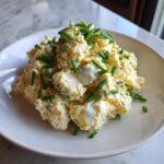 A generous serving of creamy deviled egg potato salad topped with fresh, bright green chives.