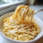 A fork lifting creamy spaghetti coated in a rich garlic parmesan sauce, topped with red pepper flakes.