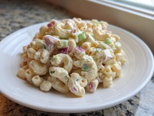 A serving of creamy macaroni salad featuring elbow pasta, chopped celery, and red onion on a white plate.