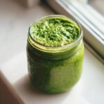 Close-up of vibrant green matcha chia pudding texture in a clear mason jar, set near a window.