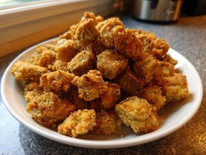 A white bowl piled high with golden brown, crispy fried okra pieces, ready to eat.