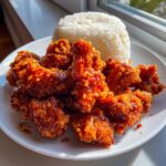 A plate of crispy, glazed orange chicken pieces served next to a mound of white rice.