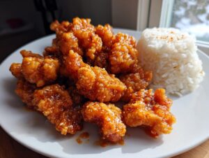 A plate of crispy, glazed orange chicken served next to a mound of steamed white rice.