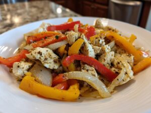 Close-up of seasoned chicken pieces mixed with sliced red, yellow, and white onions for crockpot chicken fajitas.