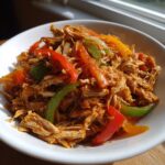 Close-up of shredded crockpot chicken fajitas mixed with colorful bell peppers in a white bowl.