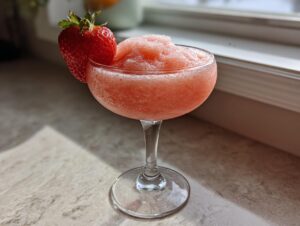 A frosty, blended strawberry daiquiri served in a coupe glass, garnished with a fresh strawberry.