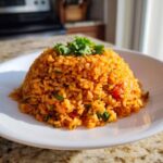 A perfectly molded mound of fluffy, orange-red Spanish rice garnished with fresh cilantro on a white plate.