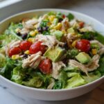 Close-up of a vibrant high protein salad featuring shredded chicken, avocado chunks, cherry tomatoes, corn, and black beans.