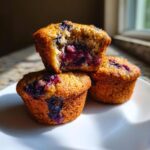 Three golden brown blueberry cottage cheese muffins stacked on a white plate, one cut open showing the moist interior.