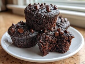 Close-up of three moist chocolate muffins topped with chocolate chips, one muffin has a bite taken out.
