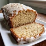 A close-up of moist eggnog bread, sliced and drizzled with a thick vanilla glaze, ready to serve.