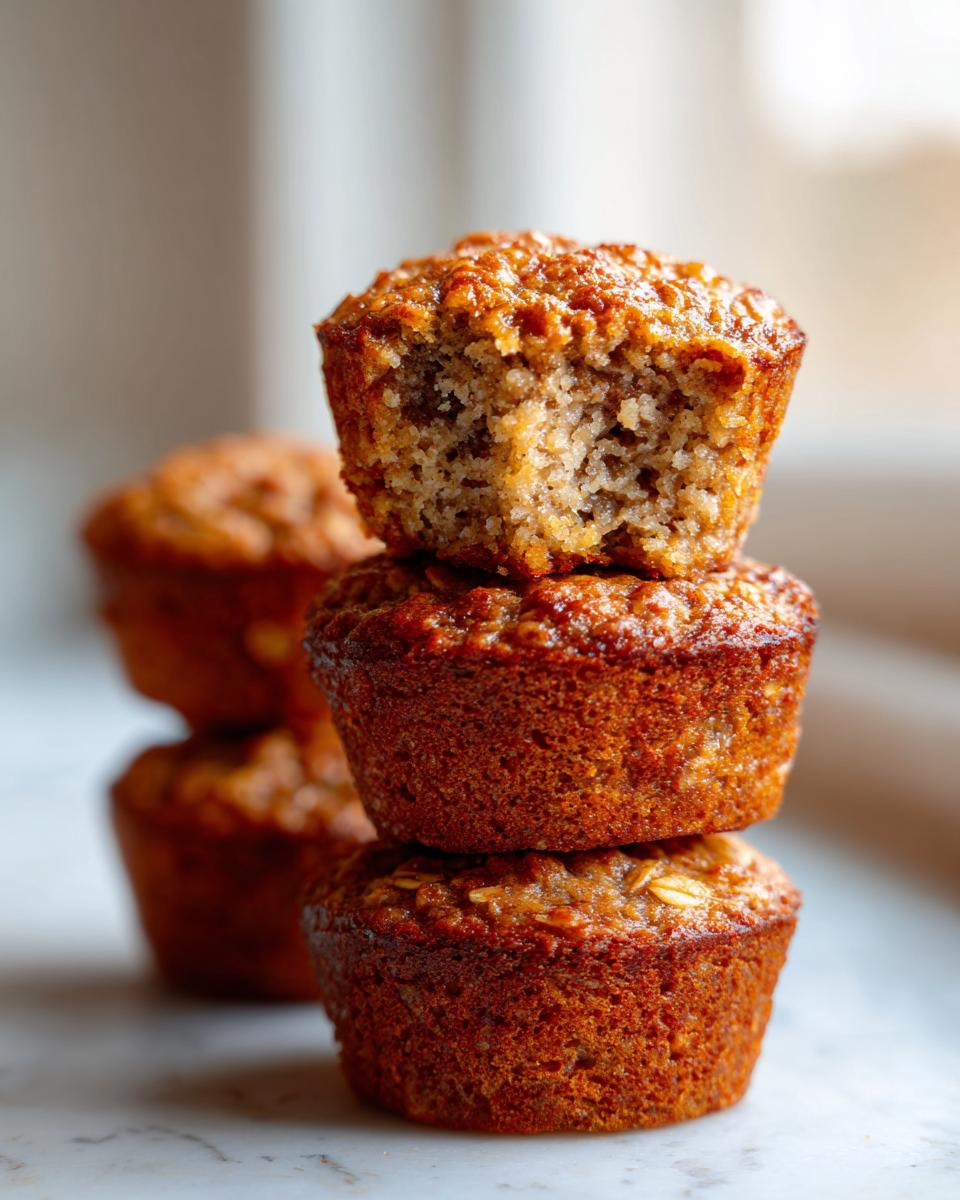 A stack of three golden brown, moist oatmeal muffins, with the top one having a bite taken out to show the texture.