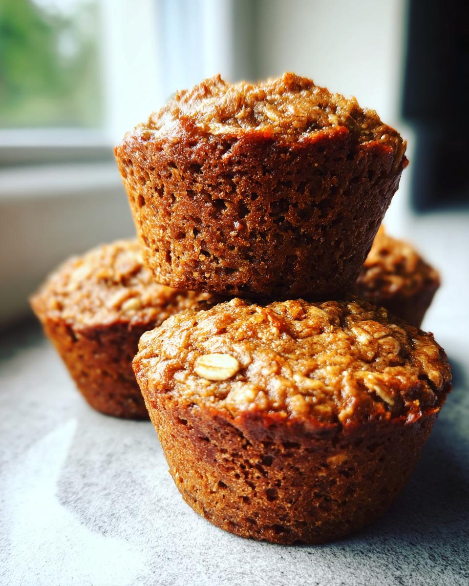 A stack of four freshly baked, moist oatmeal muffins with visible oats on top.