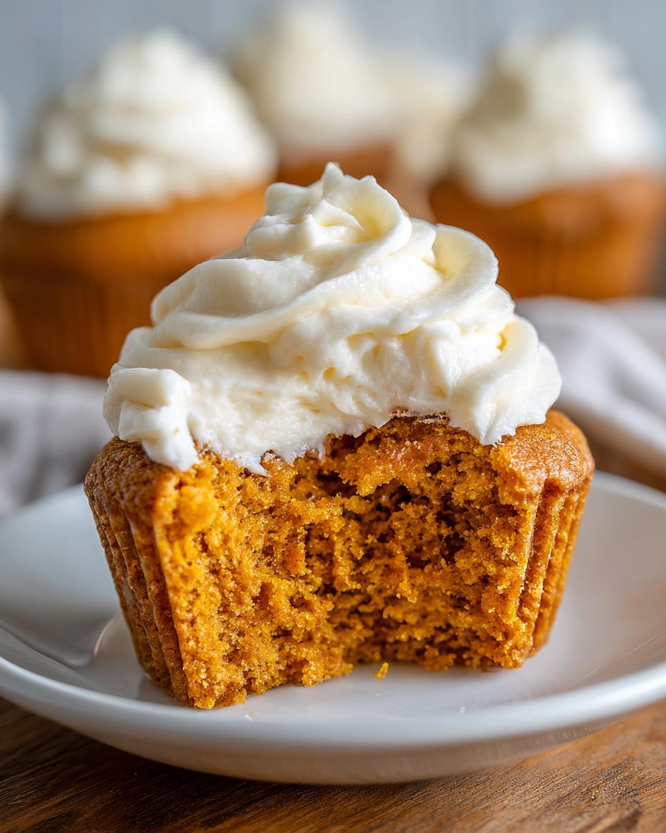 Close-up of a pumpkin spice cupcakes with a bite taken out, showing moist texture and thick cream cheese frosting.
