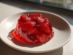 A glistening mound of bright red strawberry freezer jam, full of whole strawberry pieces, served on a small white plate.