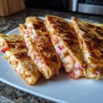 Four slices of golden brown shrimp quesadilla filled with melted cheese, shrimp, and red onion, served on a white plate.