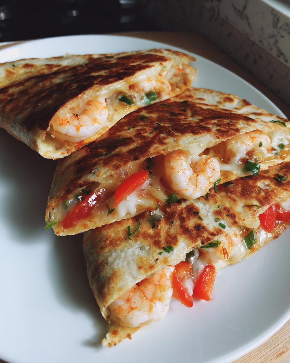 Close-up of two halves of a golden-brown shrimp quesadilla, showing melted cheese and plump shrimp filling.