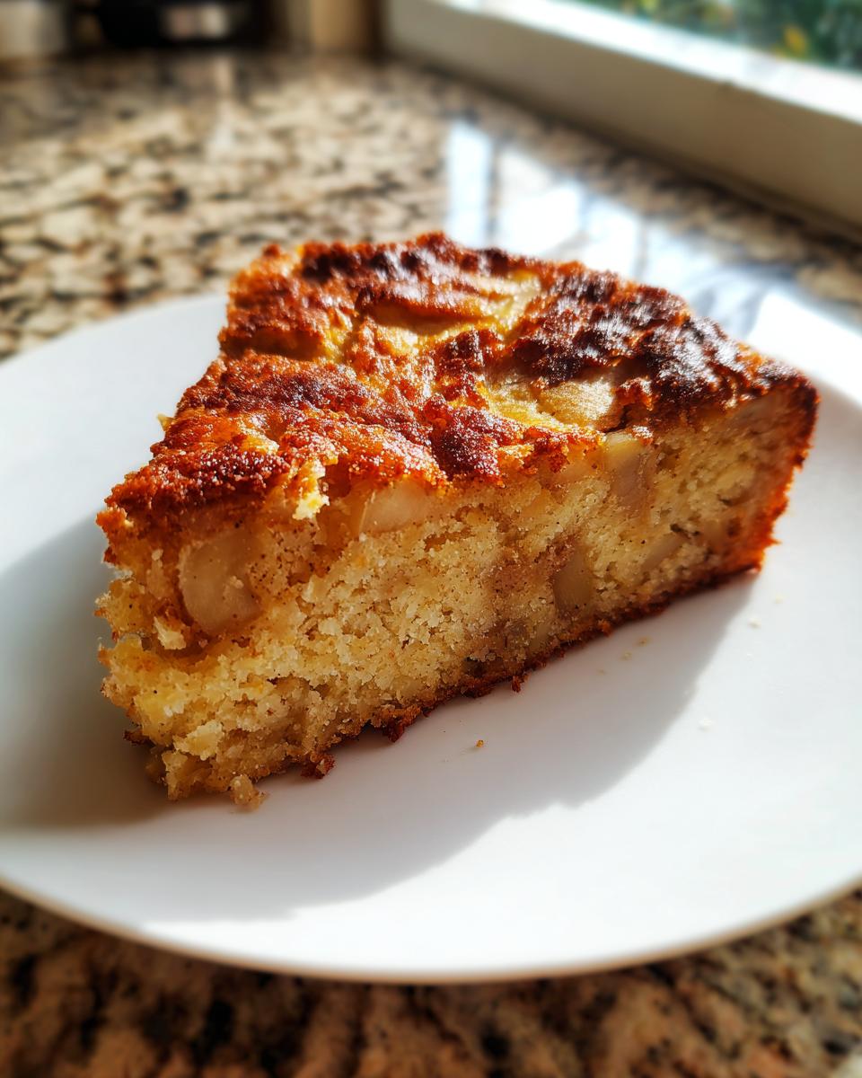 A close-up slice of moist jewish apple cake showing chunks of apple and a golden brown, slightly crisp top.