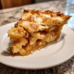 A close-up of a thick slice of homemade apple pie showing the flaky top crust and cinnamon-spiced apple filling.