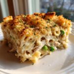 A close-up slice of creamy tuna noodle casserole topped with golden brown breadcrumbs and parsley.