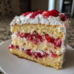 Close-up of a slice of strawberry shortcake cake showing layers of yellow cake, whipped cream, and macerated strawberries.