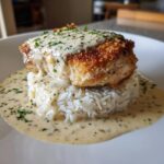 A perfectly plated serving of smothered chicken and rice, topped with creamy sauce and parsley.