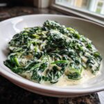 Close-up of rich, homemade creamed spinach served in a white bowl, featuring vibrant green leaves coated in a thick, creamy sauce.
