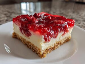 A close-up shot of a square slice of strawberry pretzel salad showing the pretzel crust, cream cheese layer, and strawberry topping.