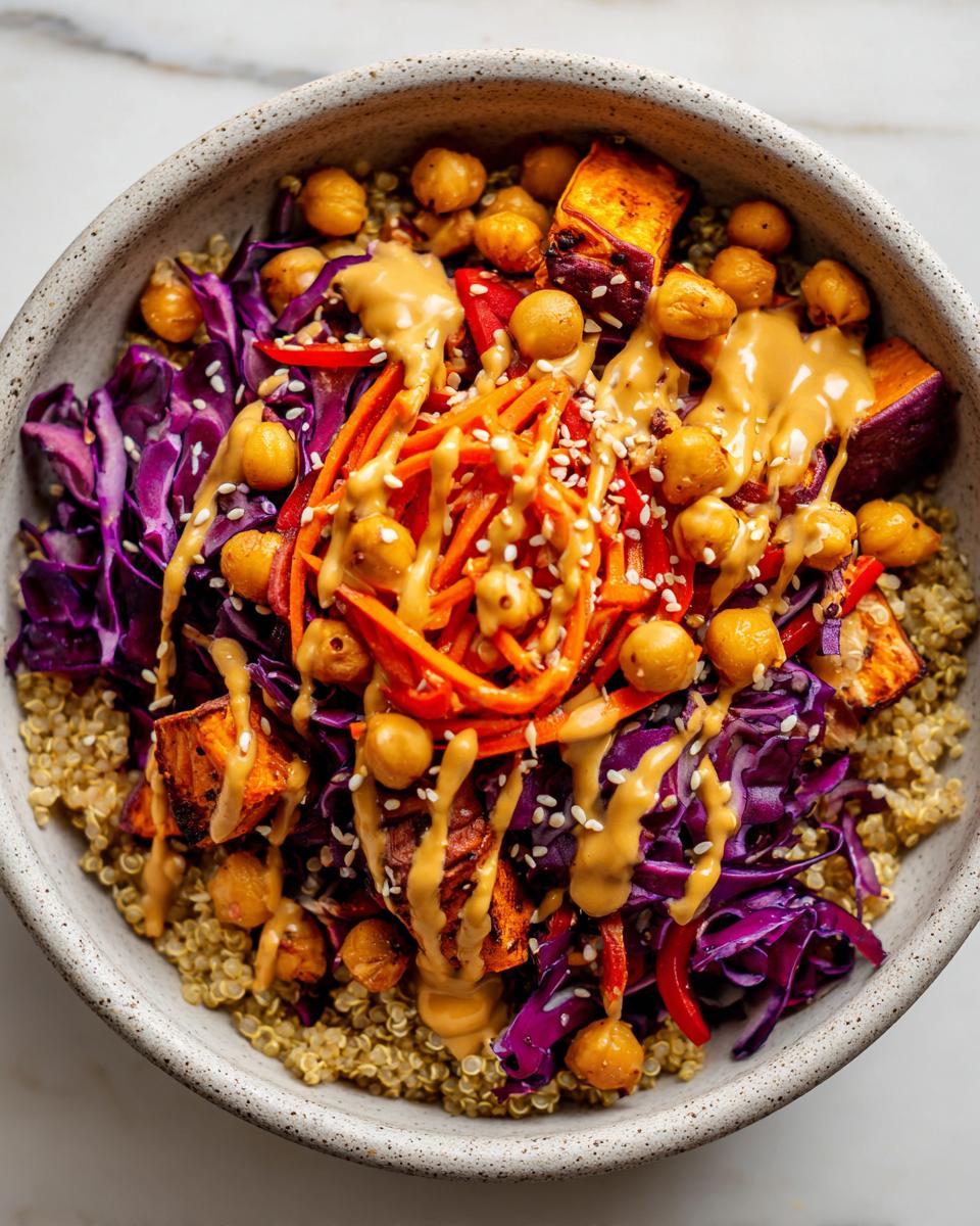 Overhead view of a colorful buddha bowl featuring quinoa, purple cabbage, roasted sweet potato, chickpeas, and peanut sauce.