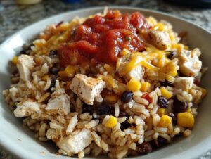 A close-up of a 30-minute chicken burrito protein bowl featuring rice, chicken chunks, black beans, corn, melted cheese, and salsa.