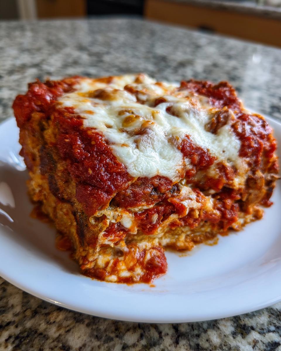 A thick, layered slice of baked eggplant parmesan covered in rich tomato sauce and melted mozzarella cheese.