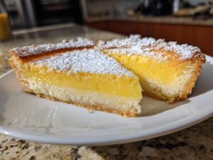 Two triangular slices of bright yellow baby lemon impossible pies, dusted heavily with powdered sugar, resting on a white plate.